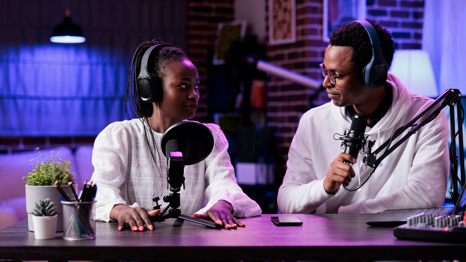 POV of man and woman recording live discussion on camera, doing podcast episode together. Lifestyle influencer talking to female guest in studio with rpg neon lights and equipment.